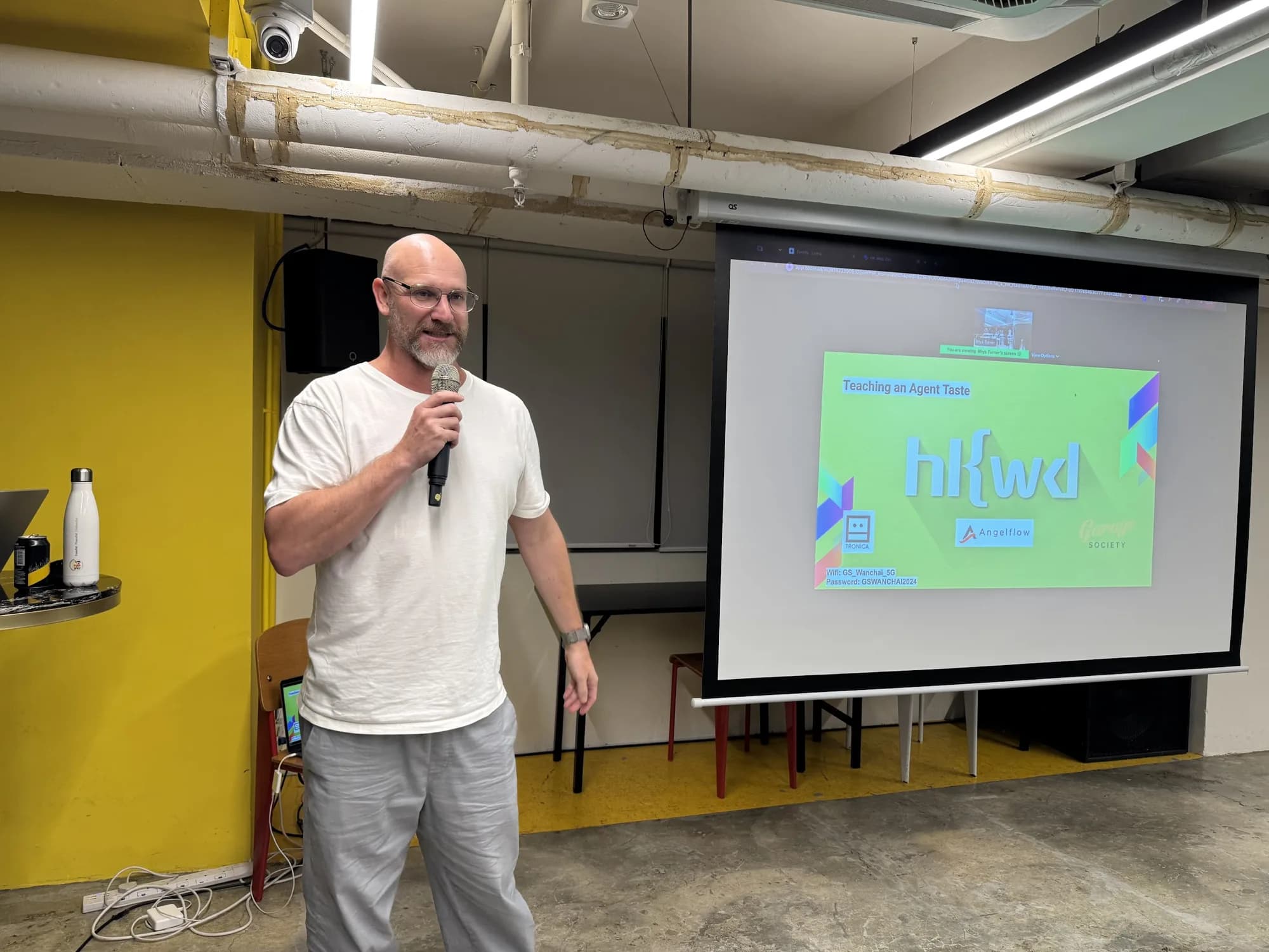 Rhys Turner speaking into a microphone beside the projector screen